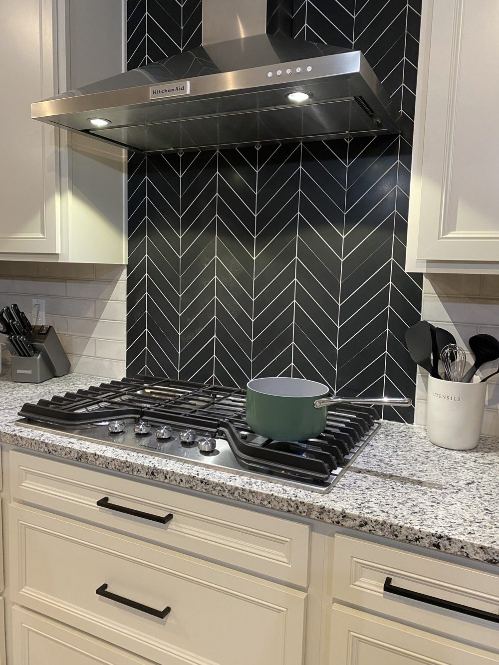Black herringbone tile backsplash behind a gas range