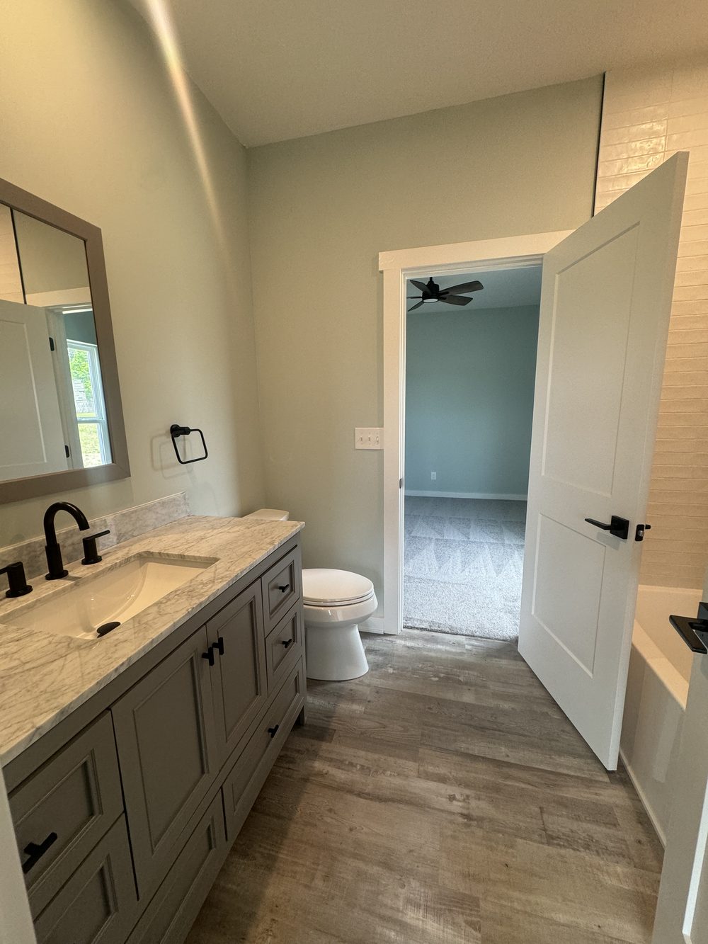 Refreshed bathroom with a new mirror, faucet, lighting and door hardware opening to a bedroom