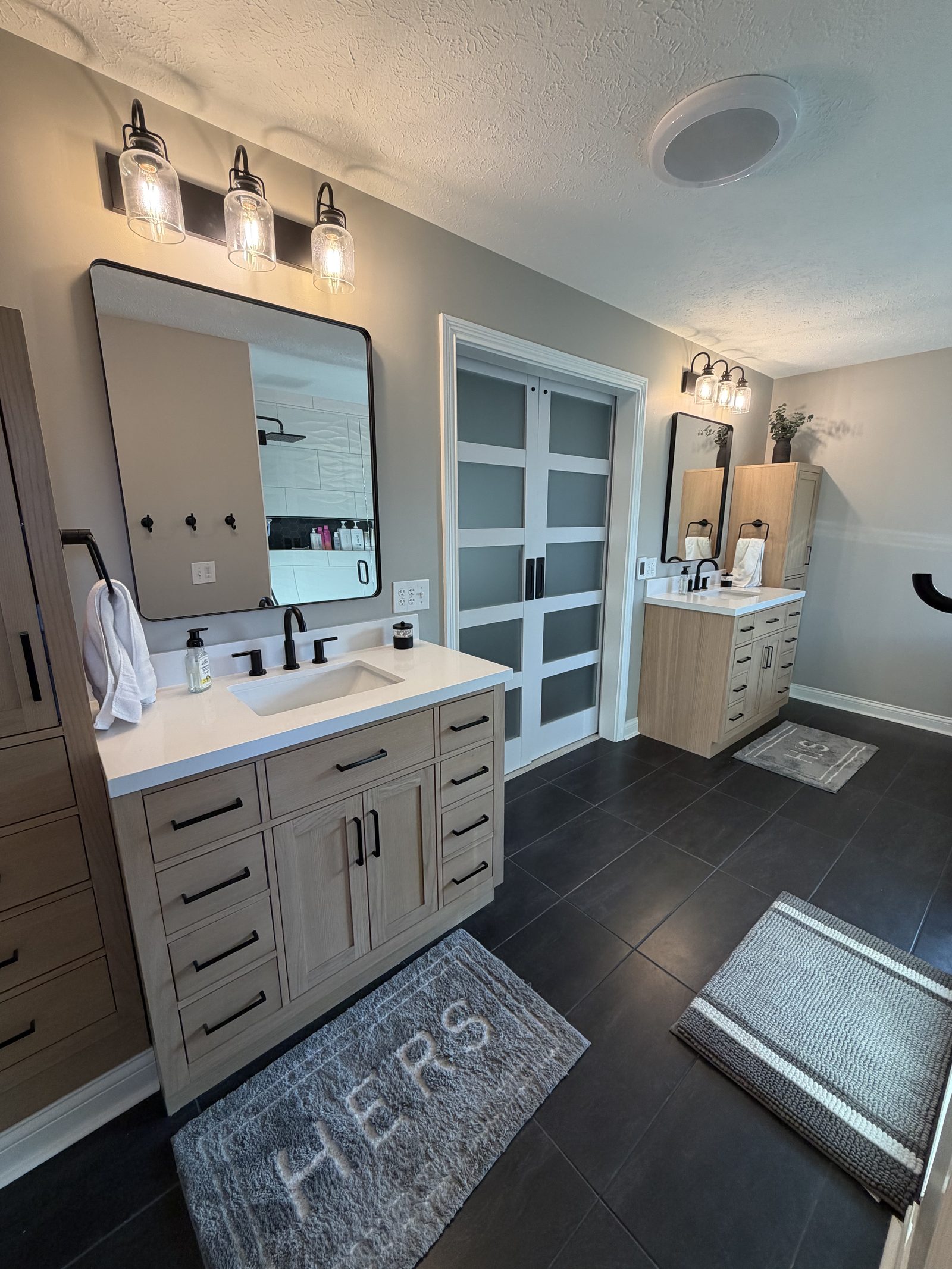 Bathroom with two separate vanities, framed mirrors and dark tile flooring