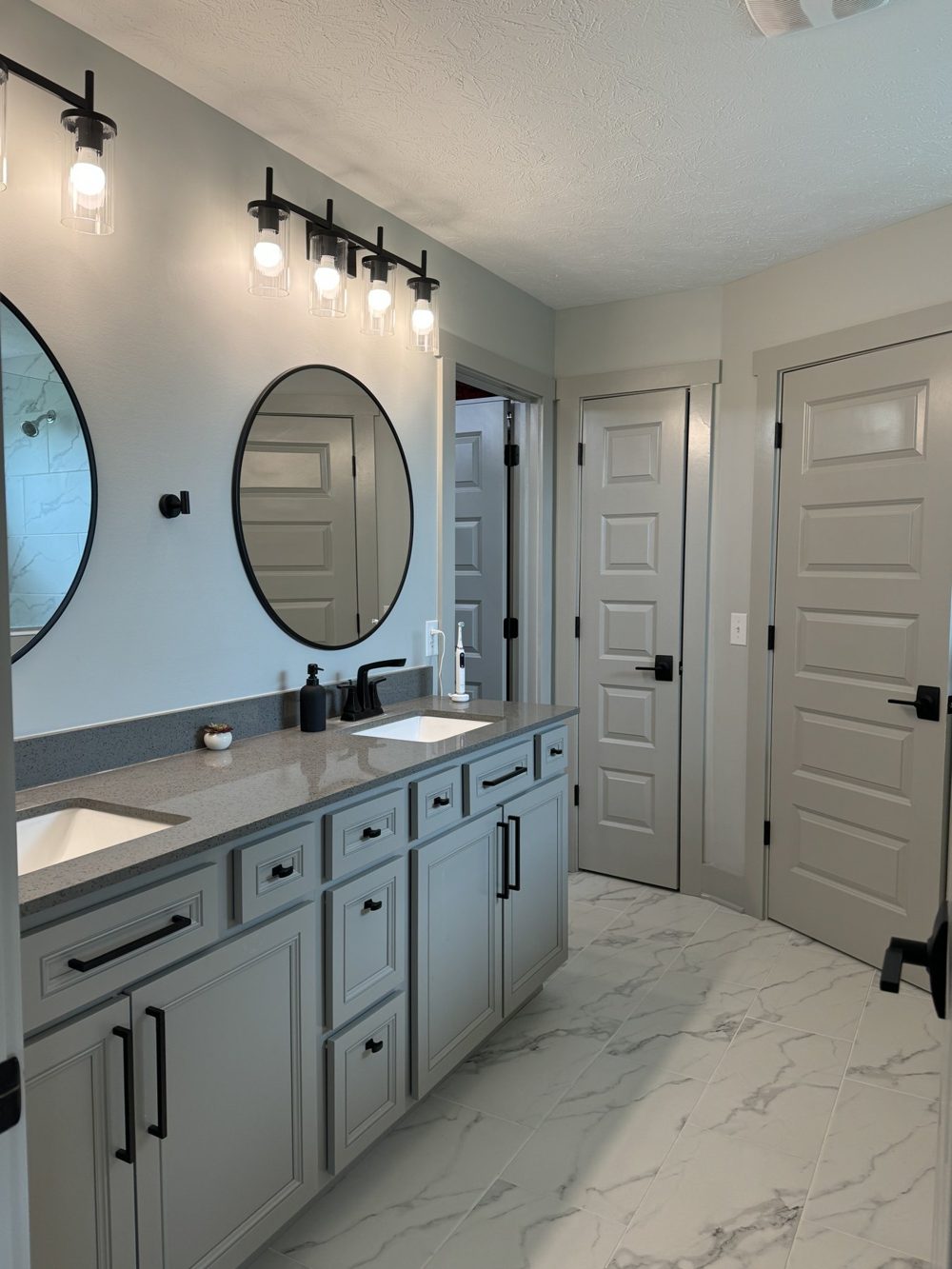 Bathroom with double vanity, round mirrors and marble look flooring