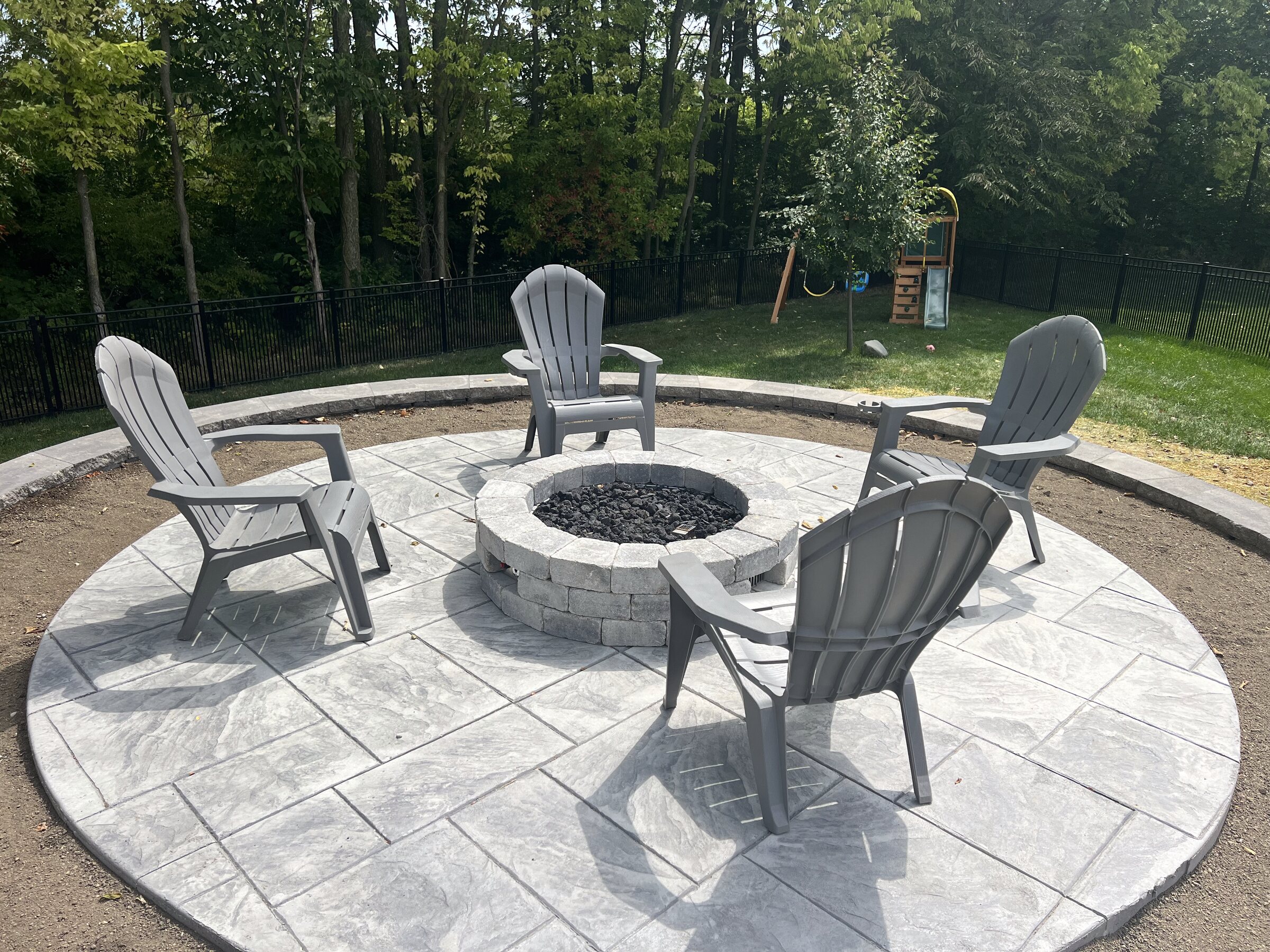 Round stamped patio with a fire pit ringed by adirondack chairs
