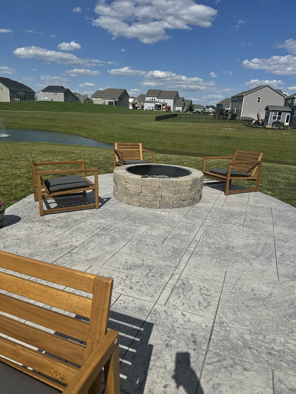 Stamped patio with a round fire pit and bench looking toward the water