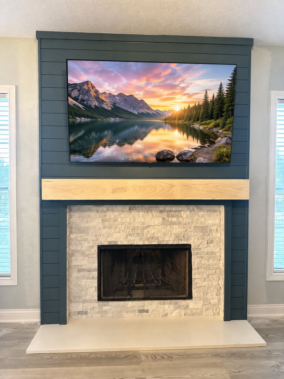 Fireplace surround finished in deep navy shiplap with a light maple beam mantel, stacked stone firebox and a mounted television