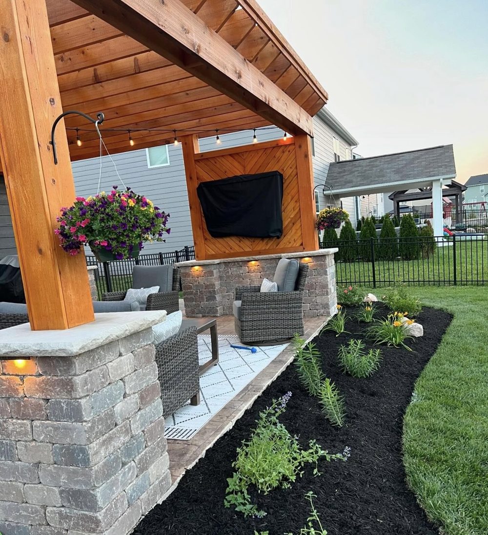 Outdoor kitchen with stone base, mounted television and planted border
