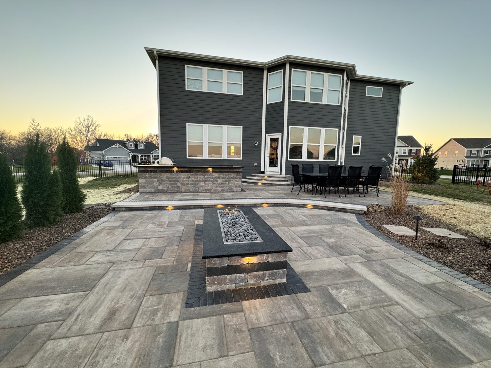 Built in outdoor kitchen and linear fire feature on a large stamped patio at sunset
