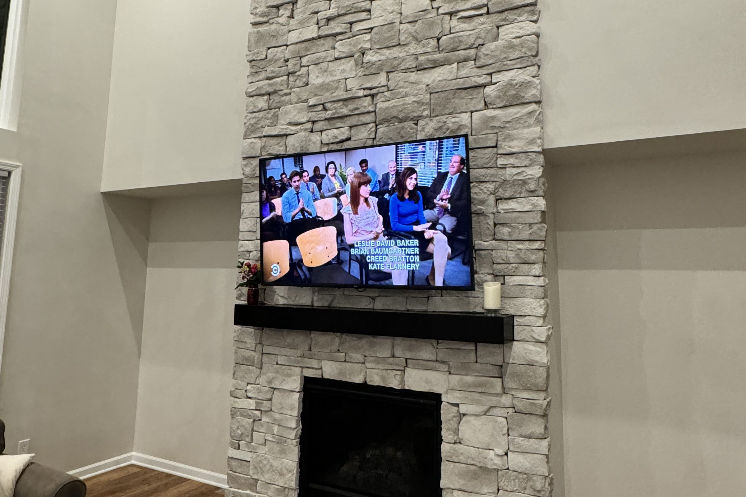 Television mounted on a floor to ceiling stacked stone fireplace with a black mantel