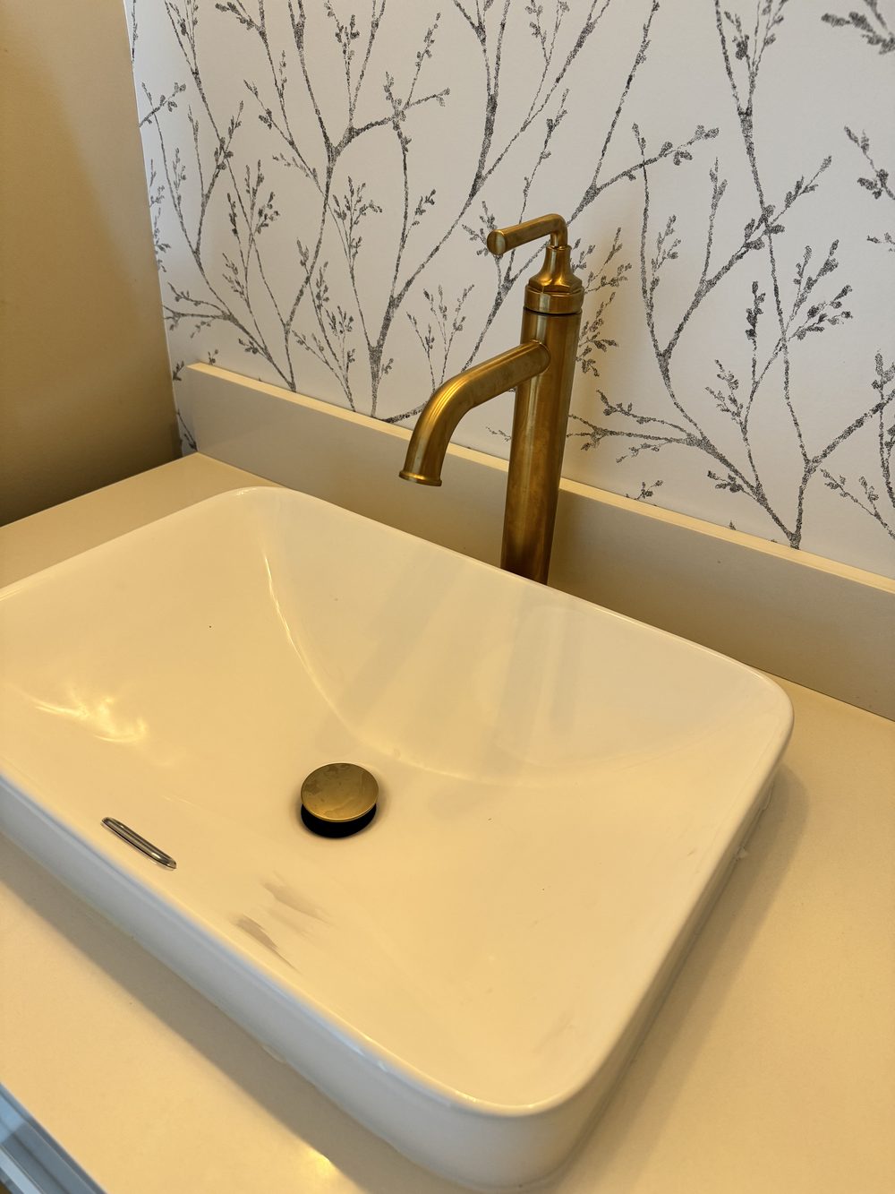 Vessel sink with a tall brushed gold faucet against patterned wallpaper